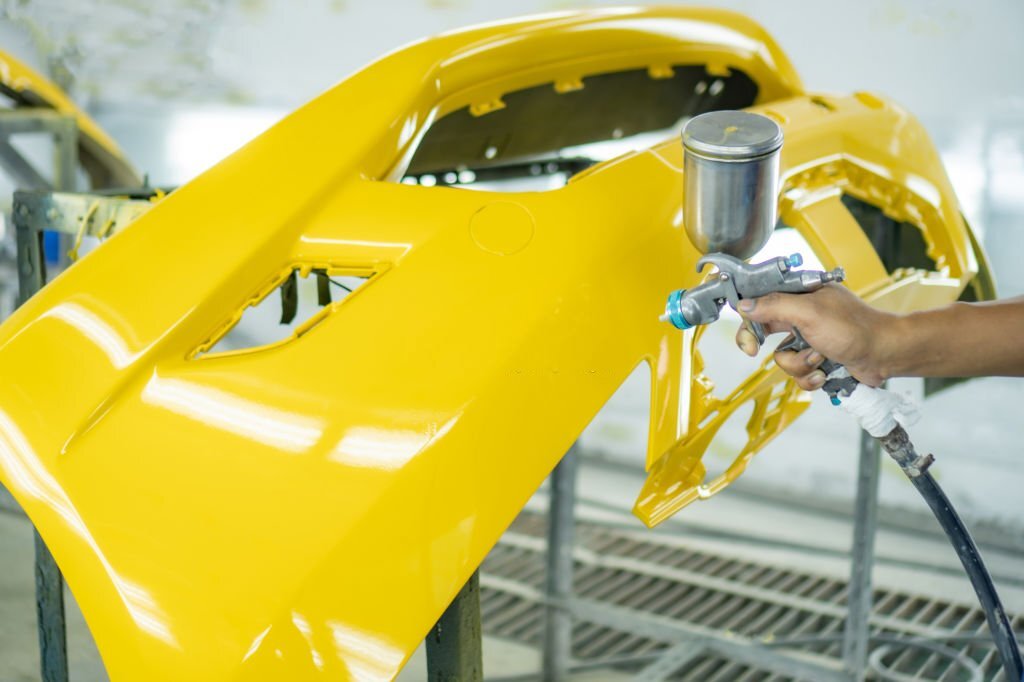 Man with protective clothes and mask painting car using spray compressor ,yellow front bumper